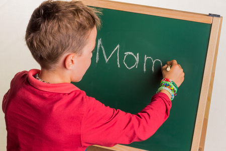 Ein Kind schreibt das Wort ' Mama ' auf eine Schultafel