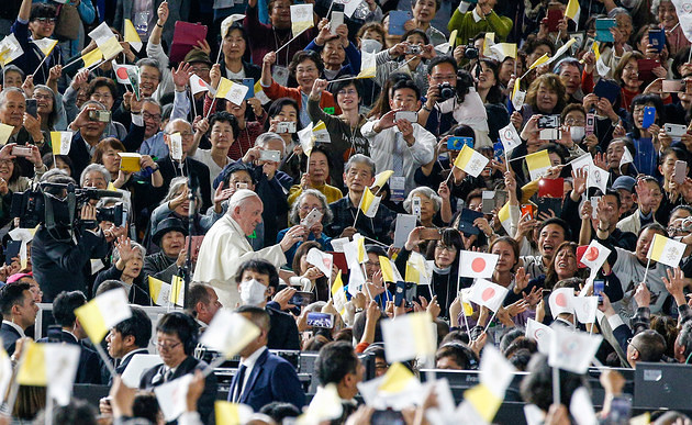 Papst Franziskus winkt den Menschen bei seiner Ankunft zu der Messe in Tokio (Japan) am 25. November 2019. Viele Besucher halten die Fahne des Vatikan hoch.