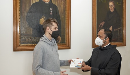 Pater Provinzial Saji Mullankuzhy überreicht in der Wiener Provinzverwaltung der Barmherzigen Brüder ein Exemplar des Buches „Kleine Gase – Große Wirkung: Der Klimawandel“ an einen Mitarbeitenden.