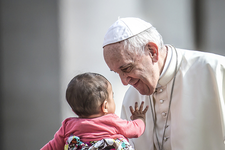 Ein Baby streckt seine Hand nach Papst Franziskus aus am 6. Juni 2018 im Vatikan. Der Papst schaut das Kind an und lächelt.