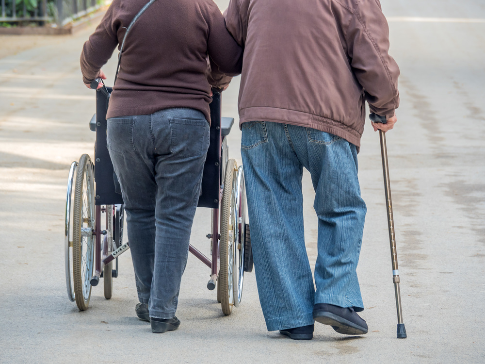 Mann und Frau gehen mit Rollstufl und Gehstock spazieren