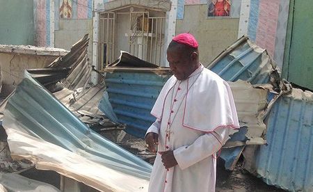 Bischof von Maiduguri (Nigeria), Oliver Dashe Doeme, vor einer zerstörten Kirche / Kirche in Not