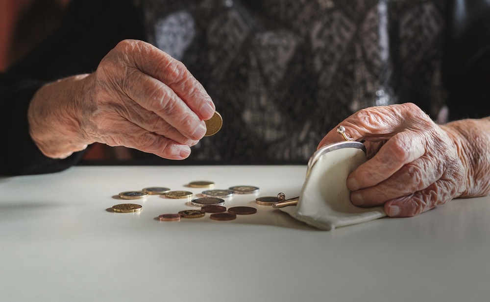 Elderly 95 years old woman sitting miserably at the table at home and counting remaining coins from the pension in her wallet after paying the bills.