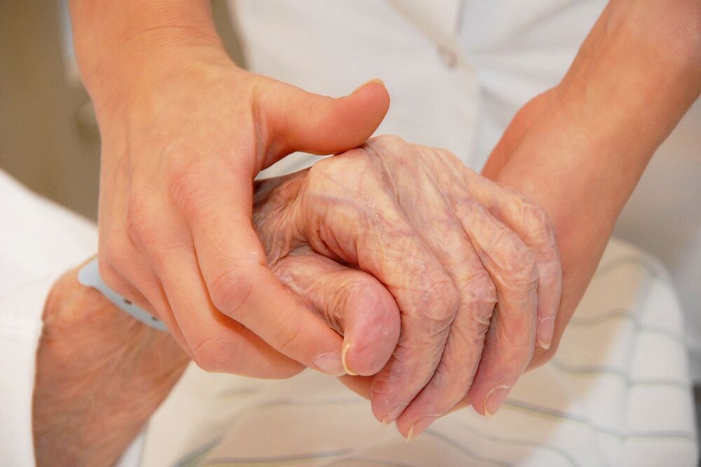 Alte Patientin reicht Pflegerin die Hand