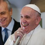 Papstreise nach Mexiko mit einem Zwischenstopp in Kuba. Bild: Papst Franziskus spricht am 12. Februar 2016 auf dem Flug nach Havanna durch ein Mikrofon. Neben ihm steht der päpstliche Reiseplaner Alberto Gasparri.