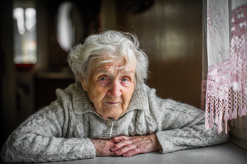 Gray-haired elderly woman sitting near the window.