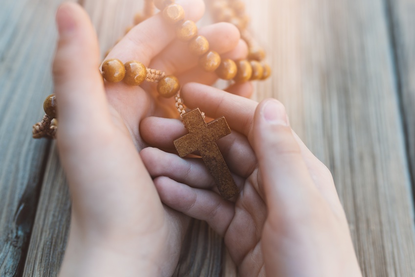 Little boy holding old wooden rosary. Child praying
