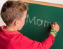 Ein Kind schreibt das Wort ' Mama ' auf eine Schultafel