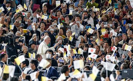 Papst Franziskus winkt den Menschen bei seiner Ankunft zu der Messe in Tokio (Japan) am 25. November 2019. Viele Besucher halten die Fahne des Vatikan hoch.