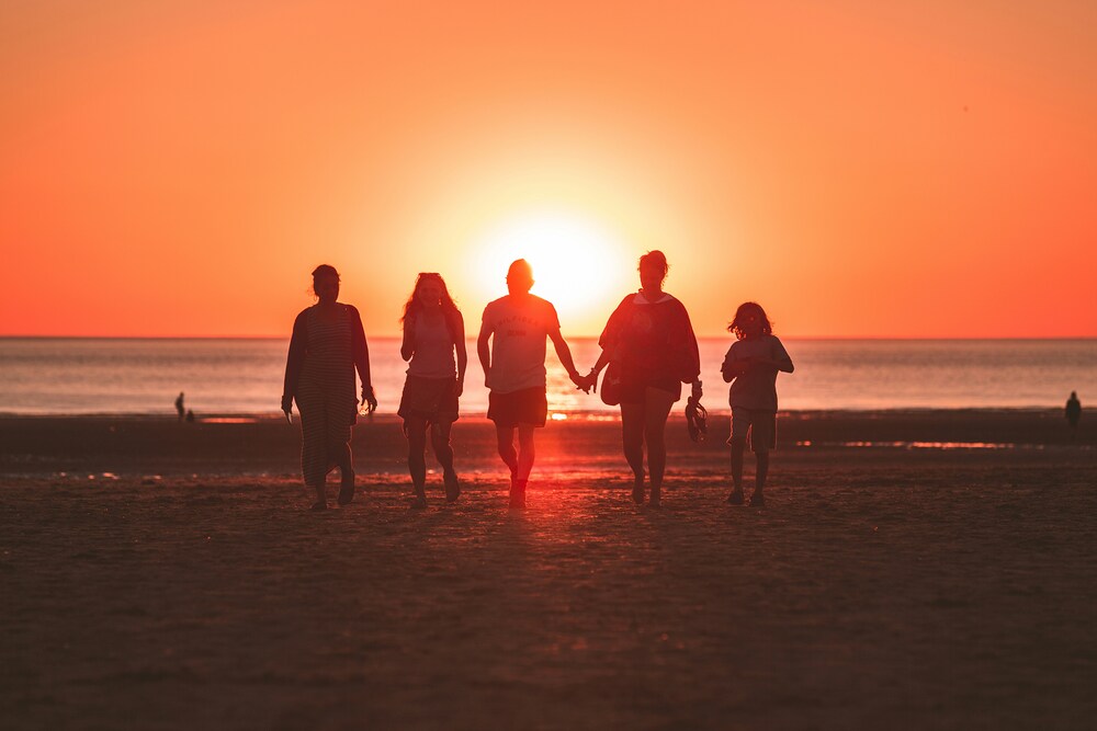 Familie im Abendrot / Foto von Kevin Delvecchio auf Unsplash Gruppe von Menschen, die am Meer steht und in die untergehende Sonne blickt