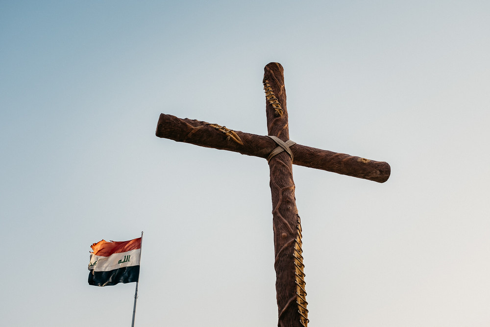 Ein großes Holzkreuz steht am Ortseingang von Karakosch (Irak) am 2. Juli 2018. Daneben weht die irakische Nationalflagge.