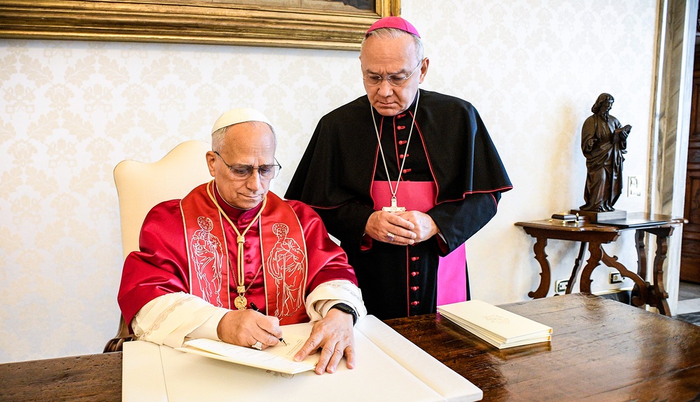 Papst Leo XIV. unterzeichnet das Apostolische Schreiben 'Dilexi te' (dt. Ich habe dich geliebt) am 4. Oktober 2025 im Vatikan. Hinter ihm steht Erzbischof Edgar Robinson Peña Parra, Substitut des Vatikanischen Staatssekretariats.