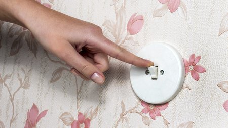 Eine Hand mit einem Lichtschalter. Licht wird ausgeschaltet.