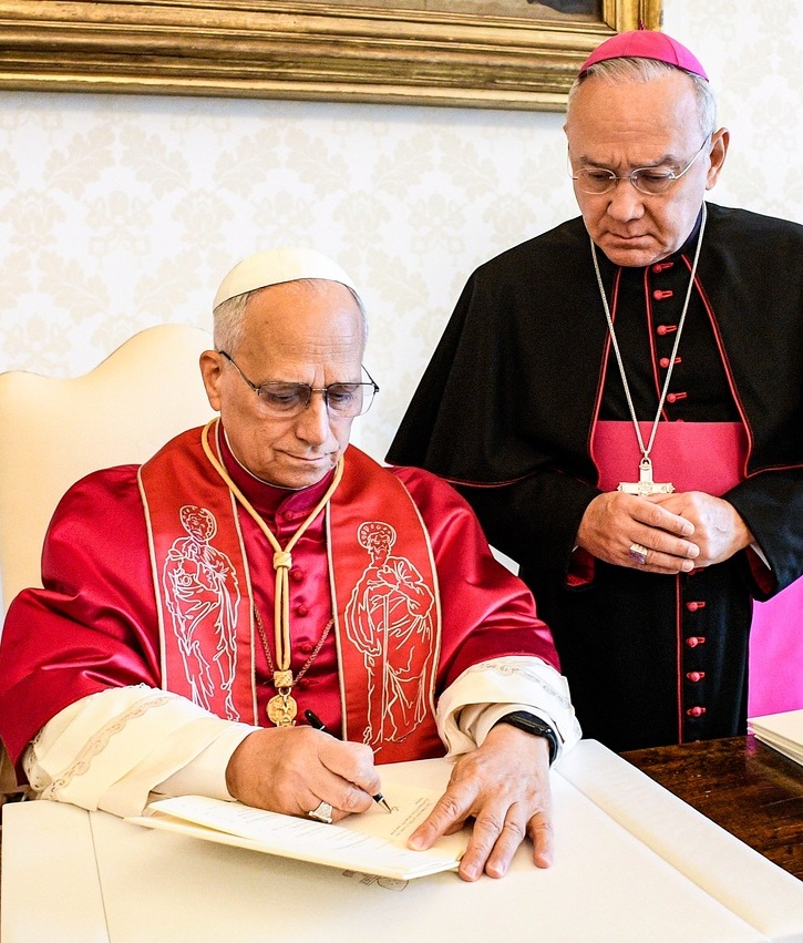 Papst Leo XIV. unterzeichnet das Apostolische Schreiben 'Dilexi te' (dt. Ich habe dich geliebt) am 4. Oktober 2025 im Vatikan. Hinter ihm steht Erzbischof Edgar Robinson Peña Parra, Substitut des Vatikanischen Staatssekretariats.