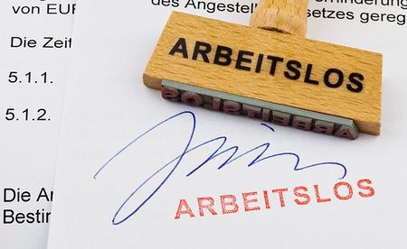 Ein Stempel aus Holz liegt auf einem Dokument. Deutsche Aufschrift: arbeitslos