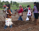 Suedamerika, Brasilien, Mato Grosso do Sul, Caarapo, 23.02.2013: Gruppe von Indigenen der Ethnie Guarani-Kaiowa mit Gesichtsbemalung und Federschmuck tanzt um Grab auf abgeerntetem Sojafeld einer besetzten Farm. Als Reaktion auf den von einem Sojafar