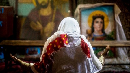 Feast of the Timkat or Baptism of the Lord in Lalibela (Ethiopia).An Ethiopian Orthodox woman prays sitting on a carpet in front of the icons of Mary and Christ in the temple of Biet Medhani Alem - House of the Saviour of the World - in Lalibela (Am