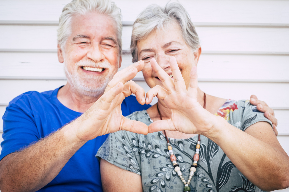 Love and valentine's day concept for cheerful happy couple of senior man and woman caucasian people together doing hearth with hands and smile - happiness after life together forever